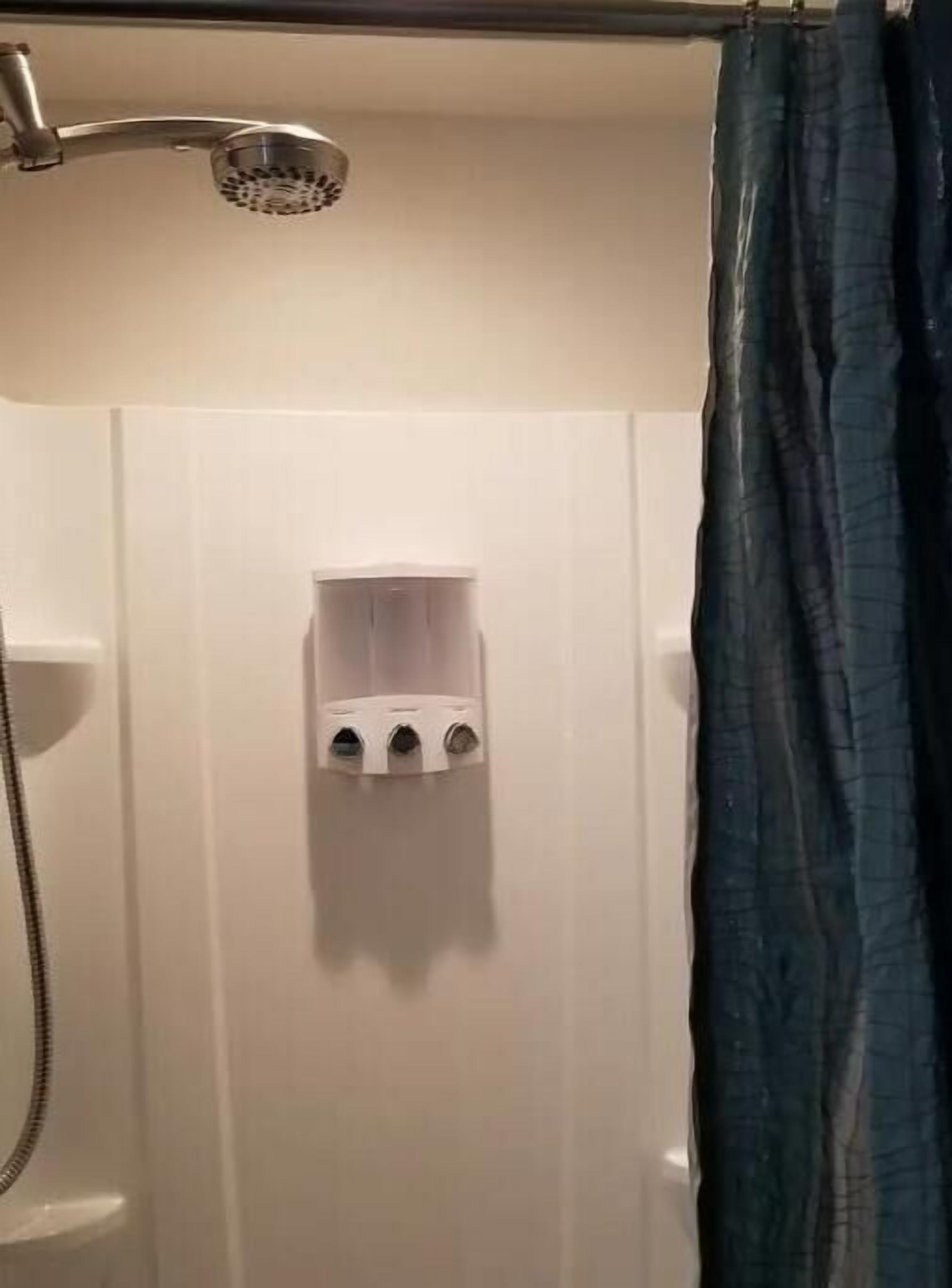 Eine Dusche mit Duschbrause und Seifenspender an der Wand.