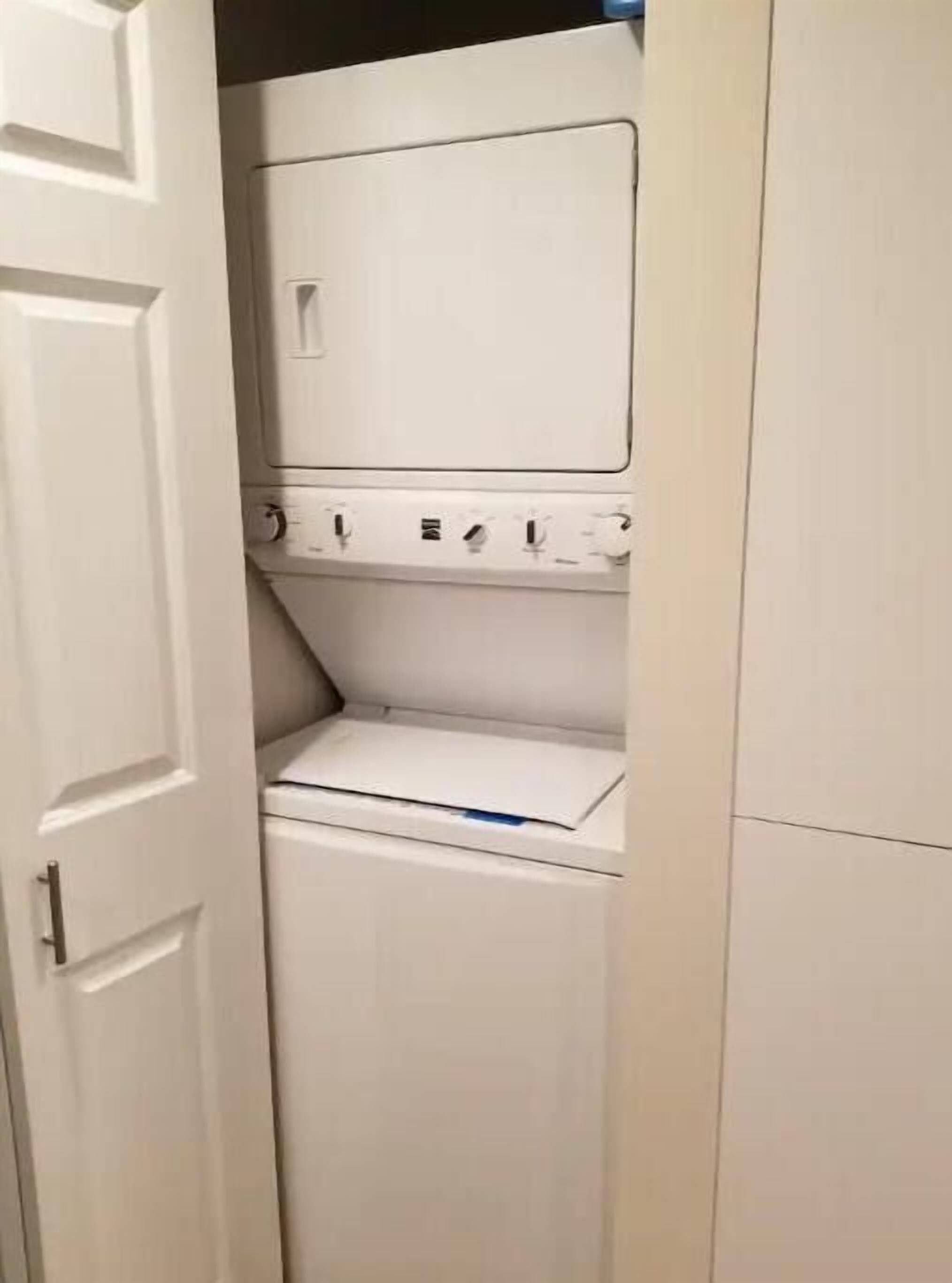 Ett kompakt, vitt tvättrum med en inbyggd tvättmaskin och torktumlare, en liten hylla och en dörr med ett handtag.