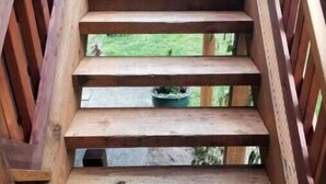 Un escalier en bois avec une rampe, menant à un espace extérieur où se trouve un conteneur vert.