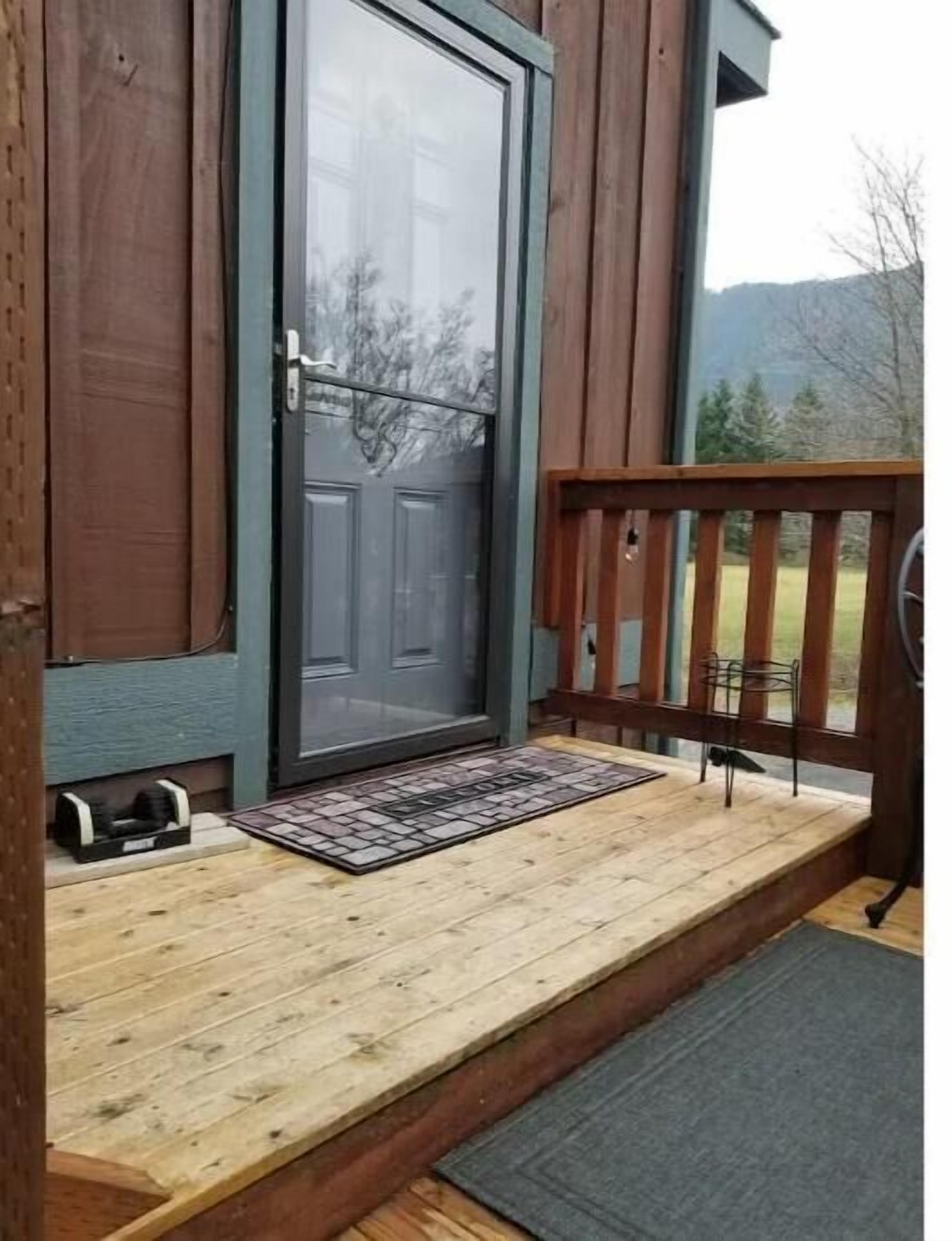 A wooden porch with a sliding glass door, a small rug, and a bench.
