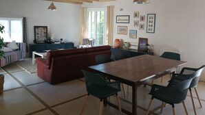 Amplia sala de estar con una mesa de comedor de madera, sillas verdes, un sofá rojo y un sillón a rayas.