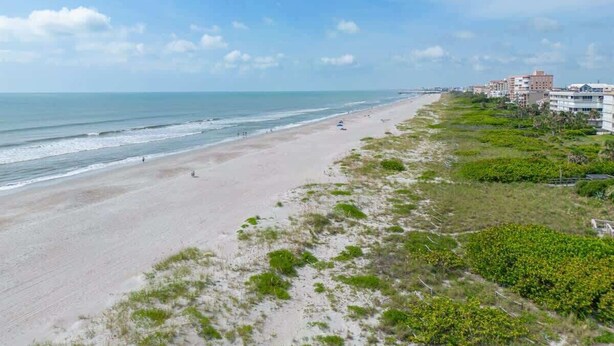 Uma praia com areal, algumas pessoas e edifícios ao fundo.