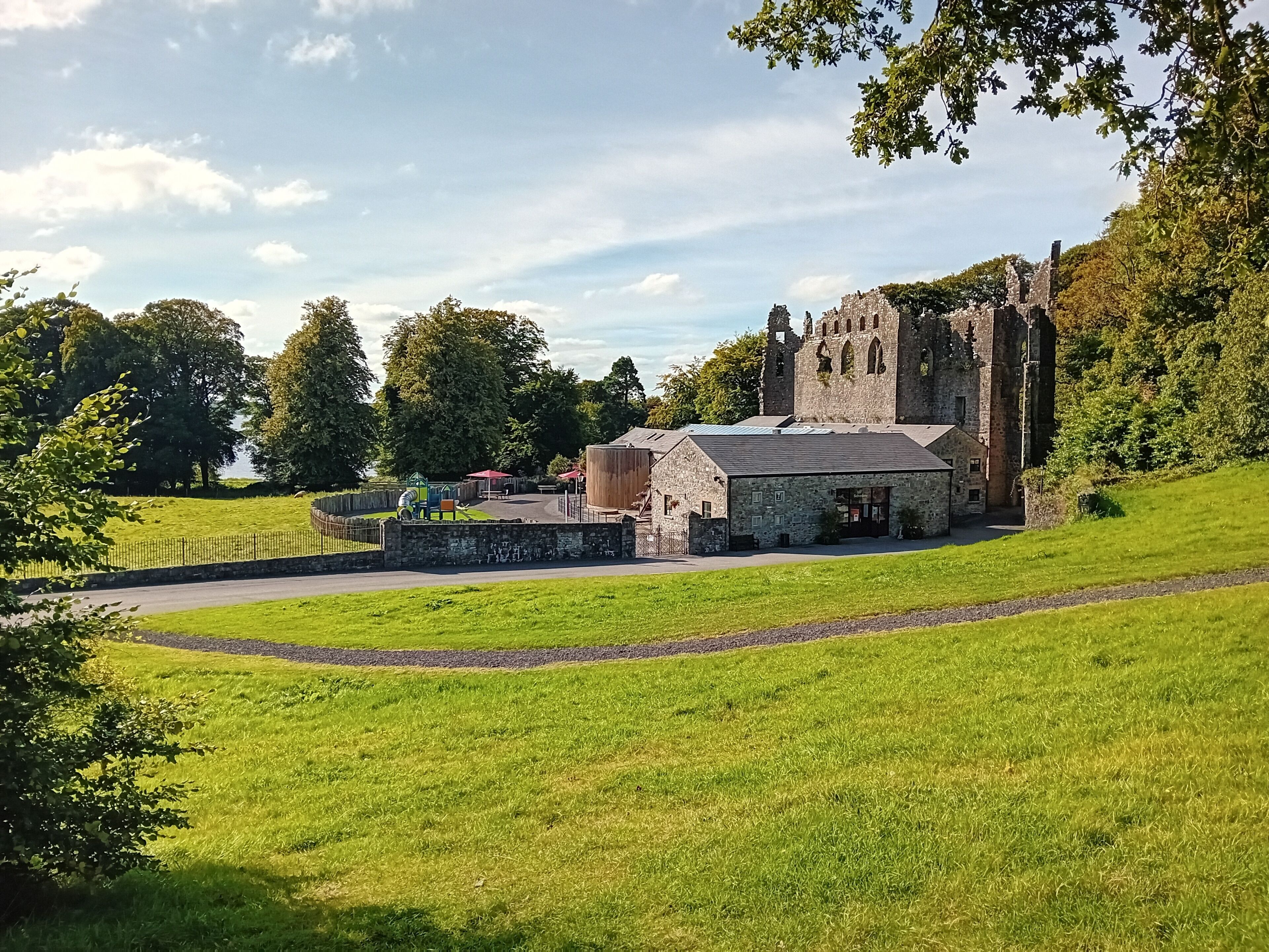 A historic stone building with a large tower, surrounded by lush green fields and trees.