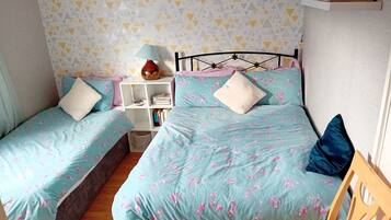 A bedroom with two single beds, a nightstand with a lamp, a small shelf, and a decorative plate on the wall.