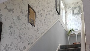 Una escalera con peldaños alfombrados de color gris y papel tapiz floral en las paredes.