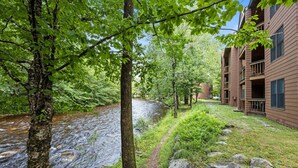 A river flowing through a wooded area with a path leading to a building with multiple balconies. - Labor Day openings! (Woodstock)