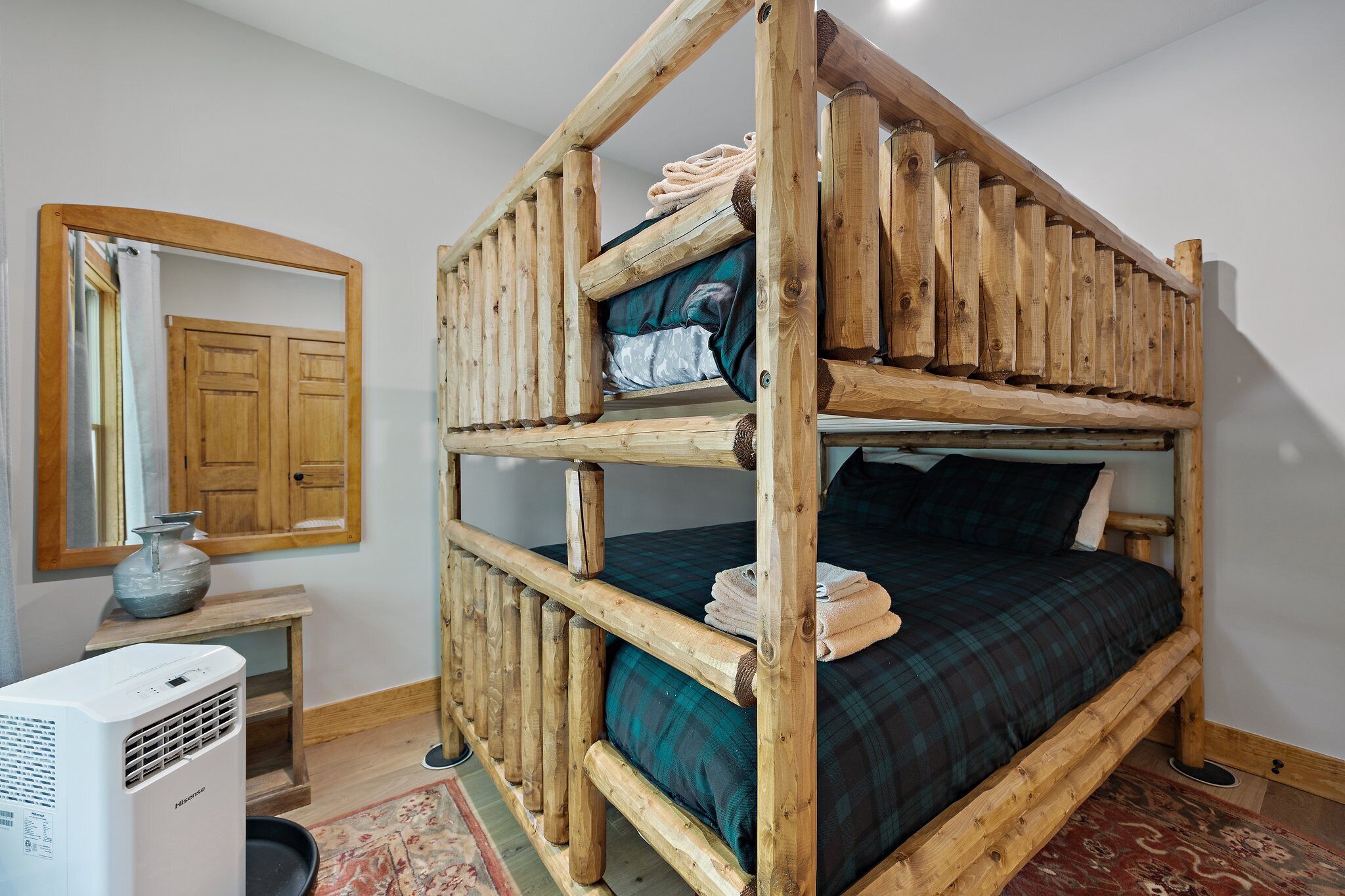 Ein Stockbett mit Holzrahmen, ein Spiegel, ein kleiner Tisch mit einer Vase und ein Heizgerät.