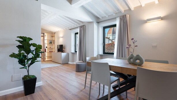 Uma zona de refeições moderna com mesa de madeira, cadeiras brancas e uma planta em vaso.