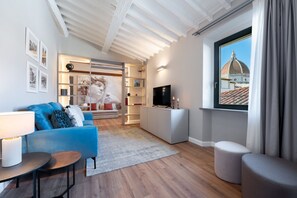 Een moderne woonkamer met een blauwe bank, een televisie, een boekenkast en uitzicht op een gebouw door een raam.