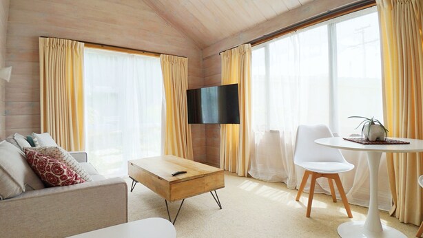 Uma sala de estar moderna com sofá, mesa de centro, mesa lateral de madeira, televisão fixada na parede e mesa de jantar com cadeiras.