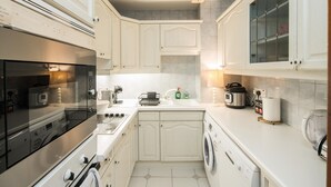 Une cuisine compacte équipée d’un four encastré, d’un lave-linge et d’une machine à café.