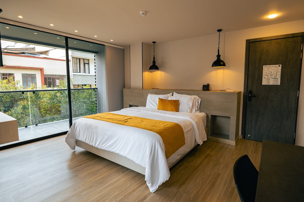 A modern bedroom with a large bed, a balcony with a view, and a desk with a chair.