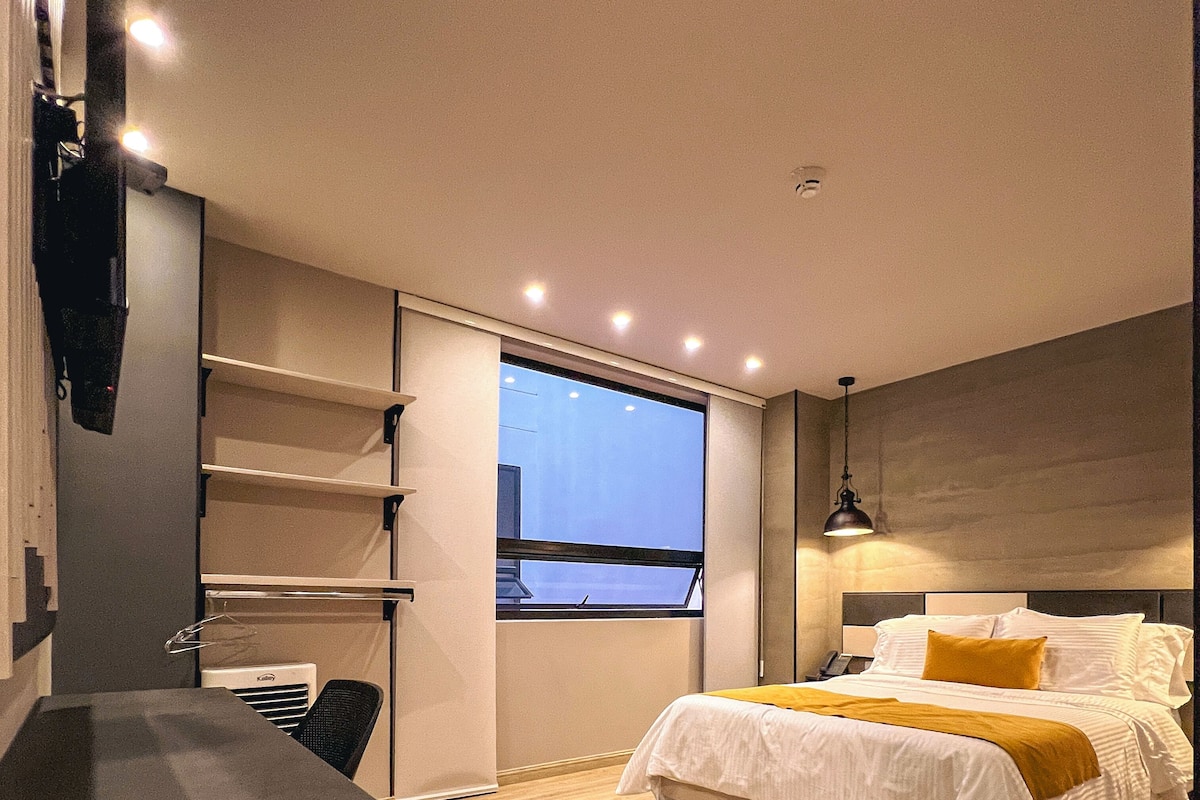 A modern bedroom with a bed, a desk, and a window.