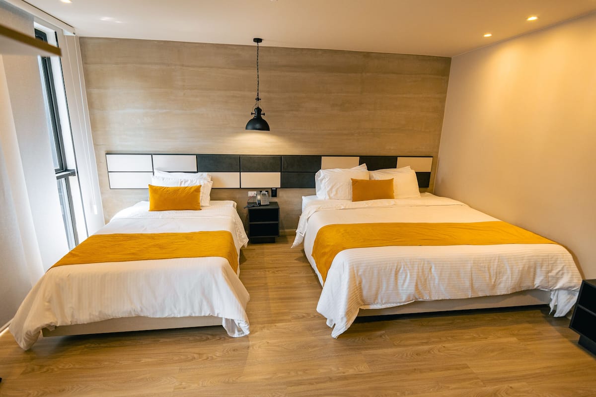 A hotel room with two beds, wooden flooring, a modern headboard, and a hanging light fixture.