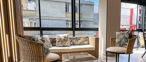 A modern living room with a sofa, two wicker chairs, a coffee table, and a large window with blinds.