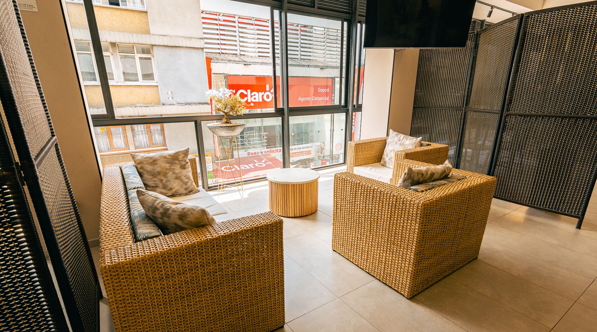 Un espace de détente moderne, doté de meubles en osier et d’une grande fenêtre donnant sur un immeuble commercial.