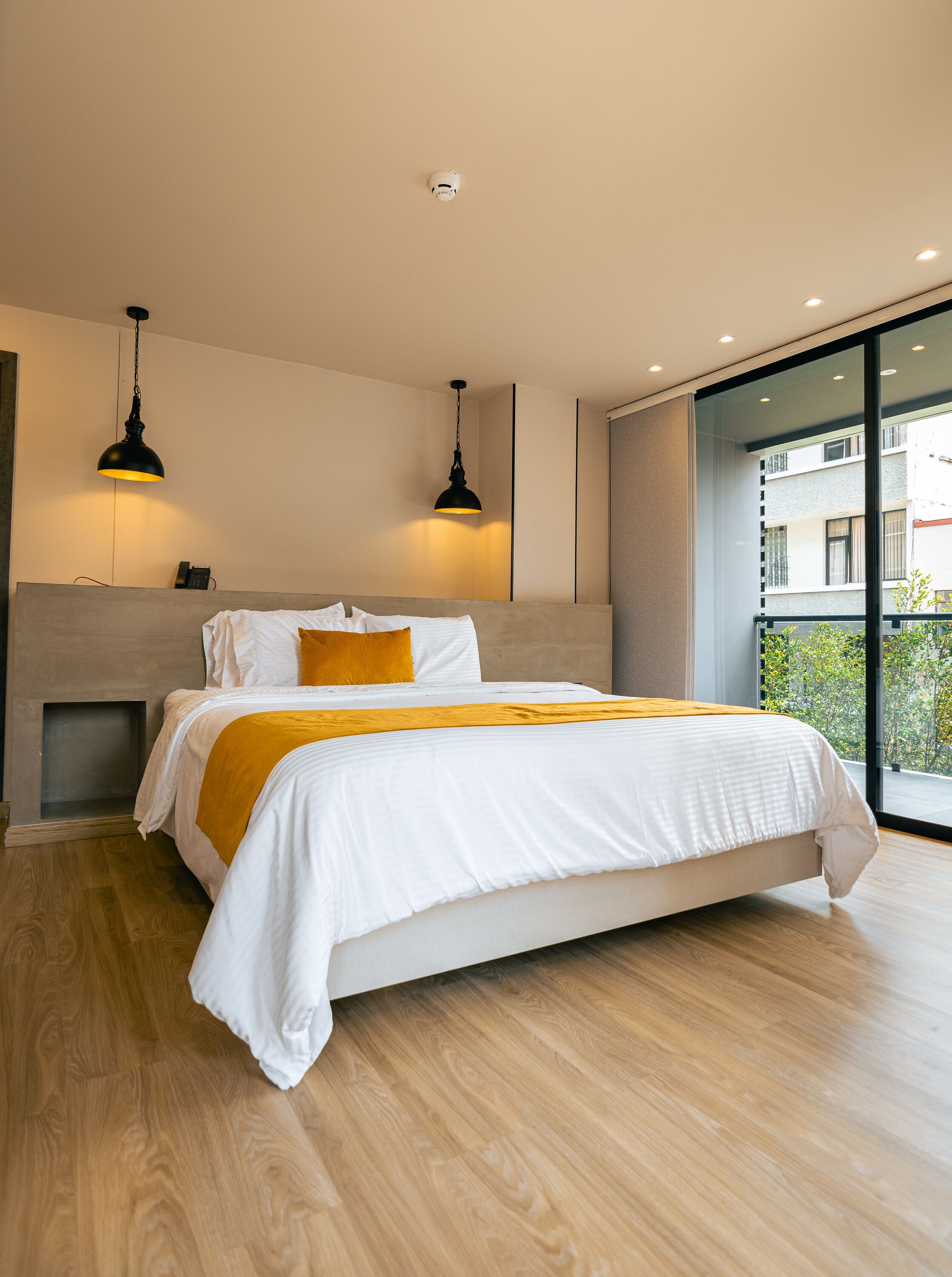 A modern bedroom with a bed, two pendant lights, a bedside table, and a view of the outside.
