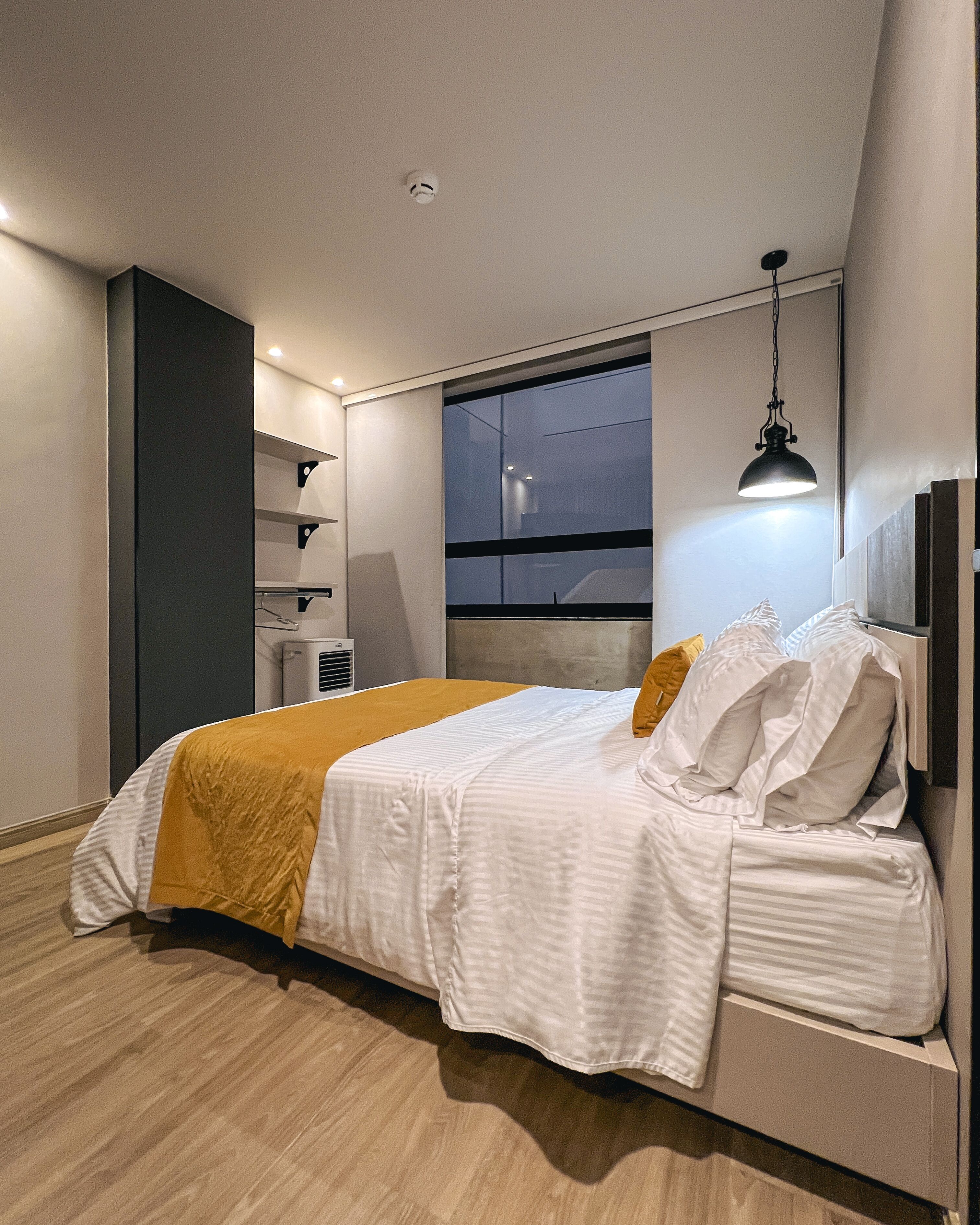 A modern bedroom with a bed, a window, and a hanging light fixture.