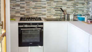 Eine Küche mit weißen Schränken, einem Gasherd, einem Backofen, einer gefliesten Spritzschutzwand und einem Spülbecken mit Geschirr.