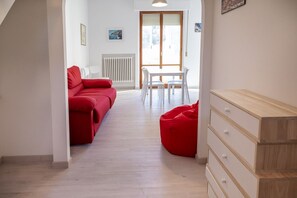 A room with a red sofa, a white table with chairs, a wooden dresser, and a radiator.