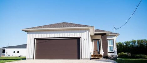 A single-story house with a brown garage door, a small porch with steps, and a clear blue sky in the background.