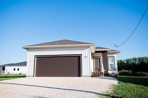 Une maison de plain-pied avec une porte de garage marron, un petit porche avec des marches et un ciel bleu clair en arrière-plan.