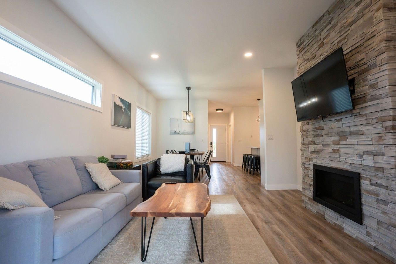 A modern living room with a sofa, coffee table, fireplace, and a TV mounted on a stone wall.