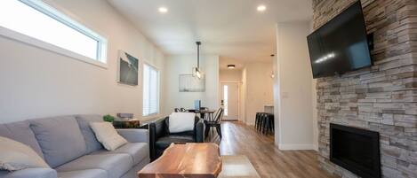 A modern living room with a sofa, coffee table, fireplace, and a TV mounted on a stone wall.
