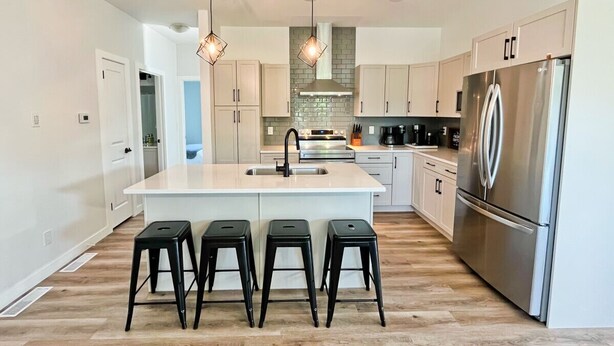 A modern kitchen with a central island, stainless steel appliances, and a herringbone wood floor.
