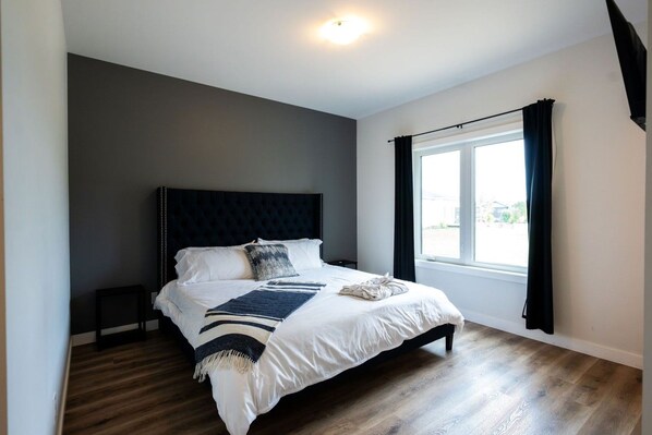 A bedroom with a large bed, dark headboard, and a window with curtains.