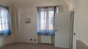 Een slaapkamer met een bed, een radiator, een deur en een raam met gordijnen.