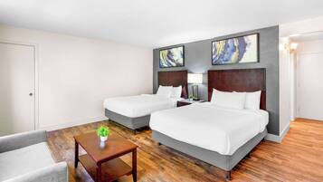 Quarto de hotel com duas camas, uma mesinha com uma planta e um sofá cinzento.