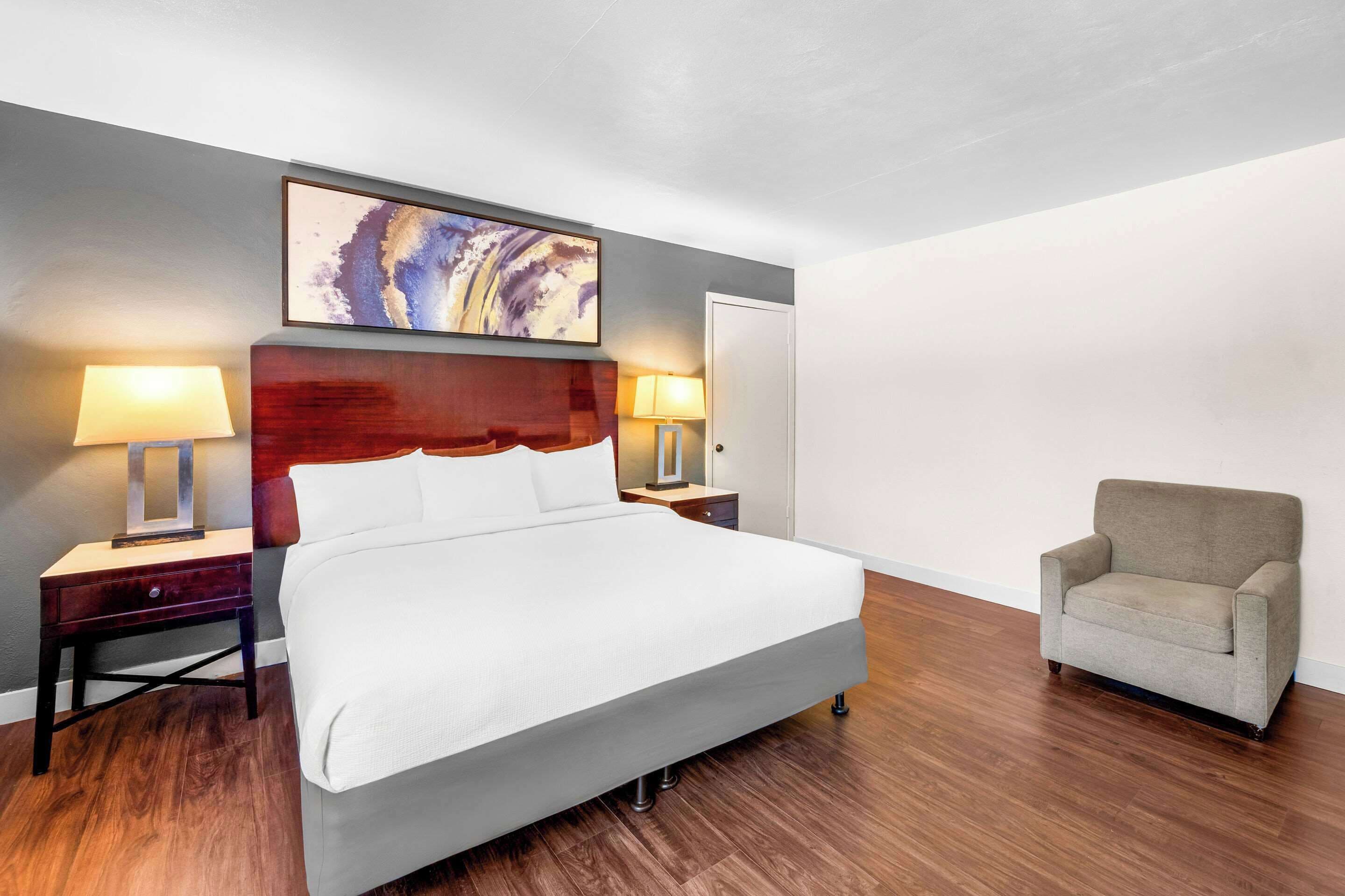 A hotel room with a large bed, two bedside tables with lamps, a chair, and a painting on the wall.