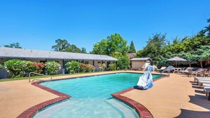A swimming pool with a brick edge, lounge chairs, and a covered area with an umbrella. - Quality Inn & Suites Jackson (Jackson)