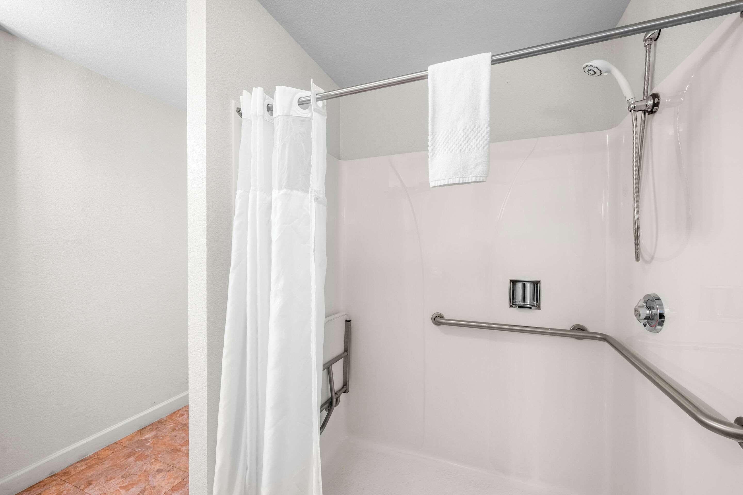 A shower area with a white shower curtain, a handheld showerhead, and a handheld faucet.