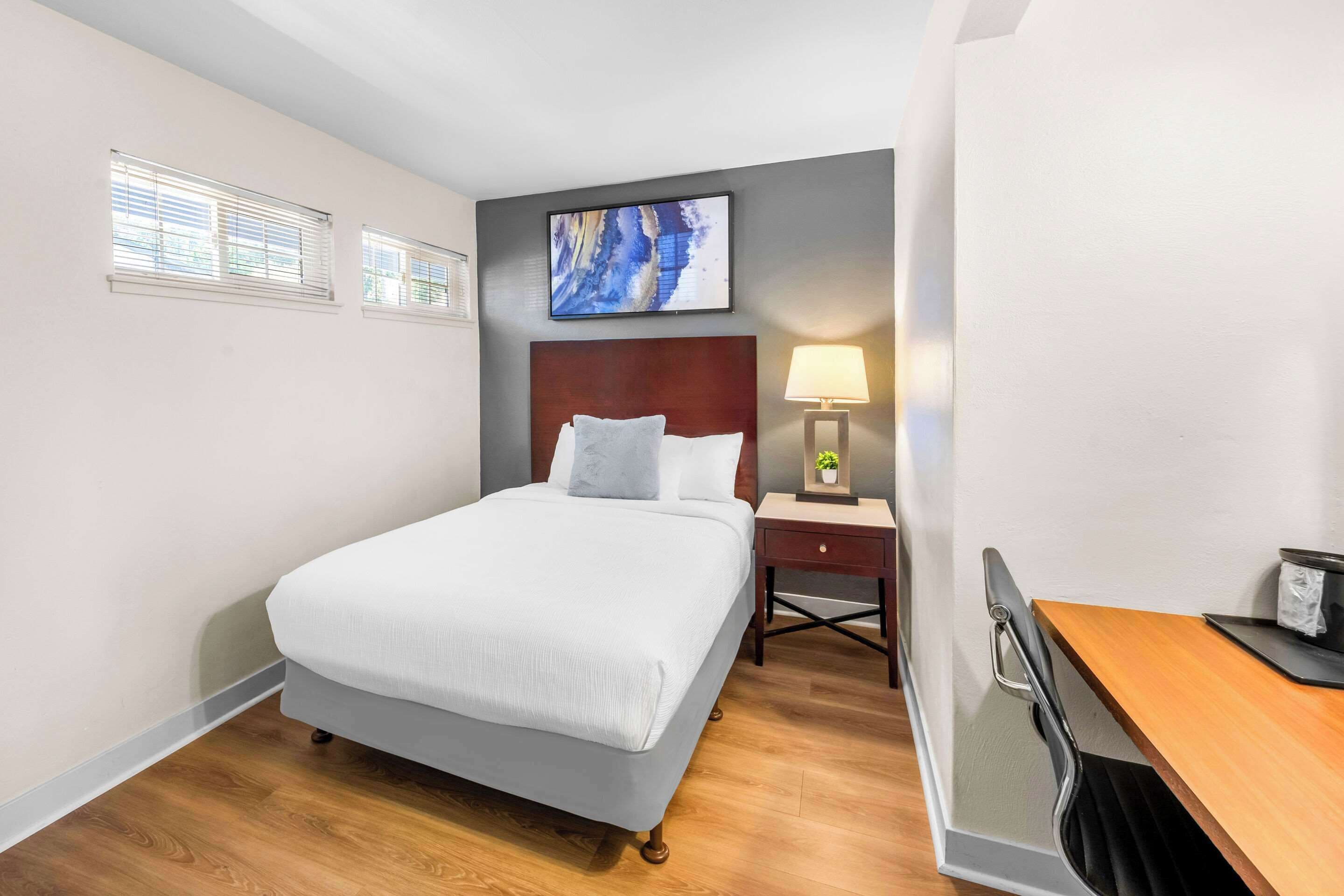 A hotel room with a bed, a nightstand, a desk, and a painting on the wall.