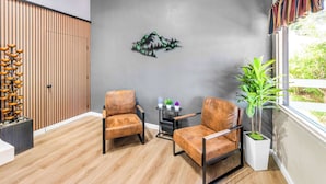 A modern room with two leather chairs, a wooden floor, a wall-mounted decorative piece, a small table with plants, and a large window with a view of greenery. - Quality Inn & Suites Jackson (Jackson)