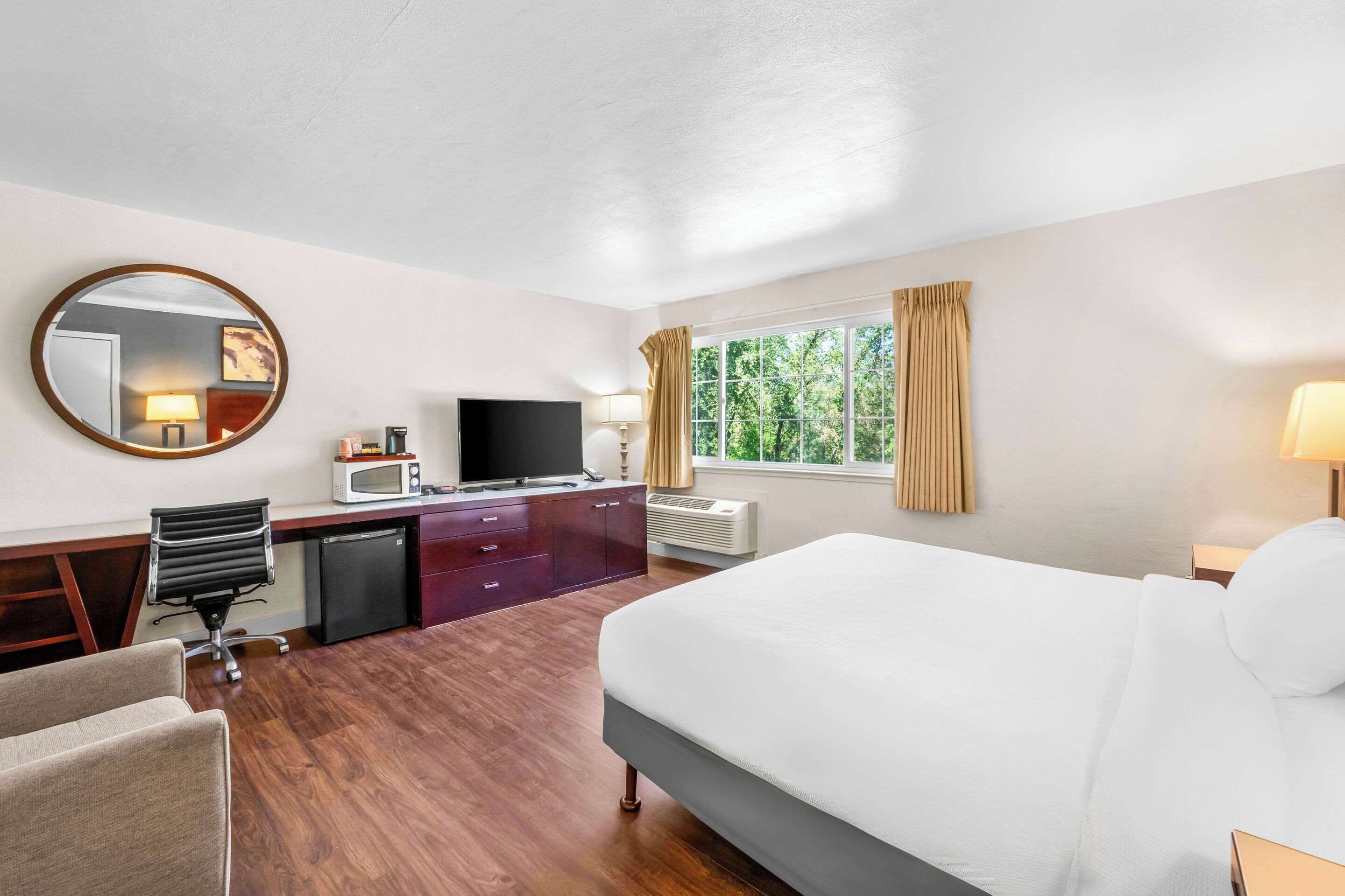 Una habitación de hotel con cama, escritorio, silla, televisor y ventana con cortinas.