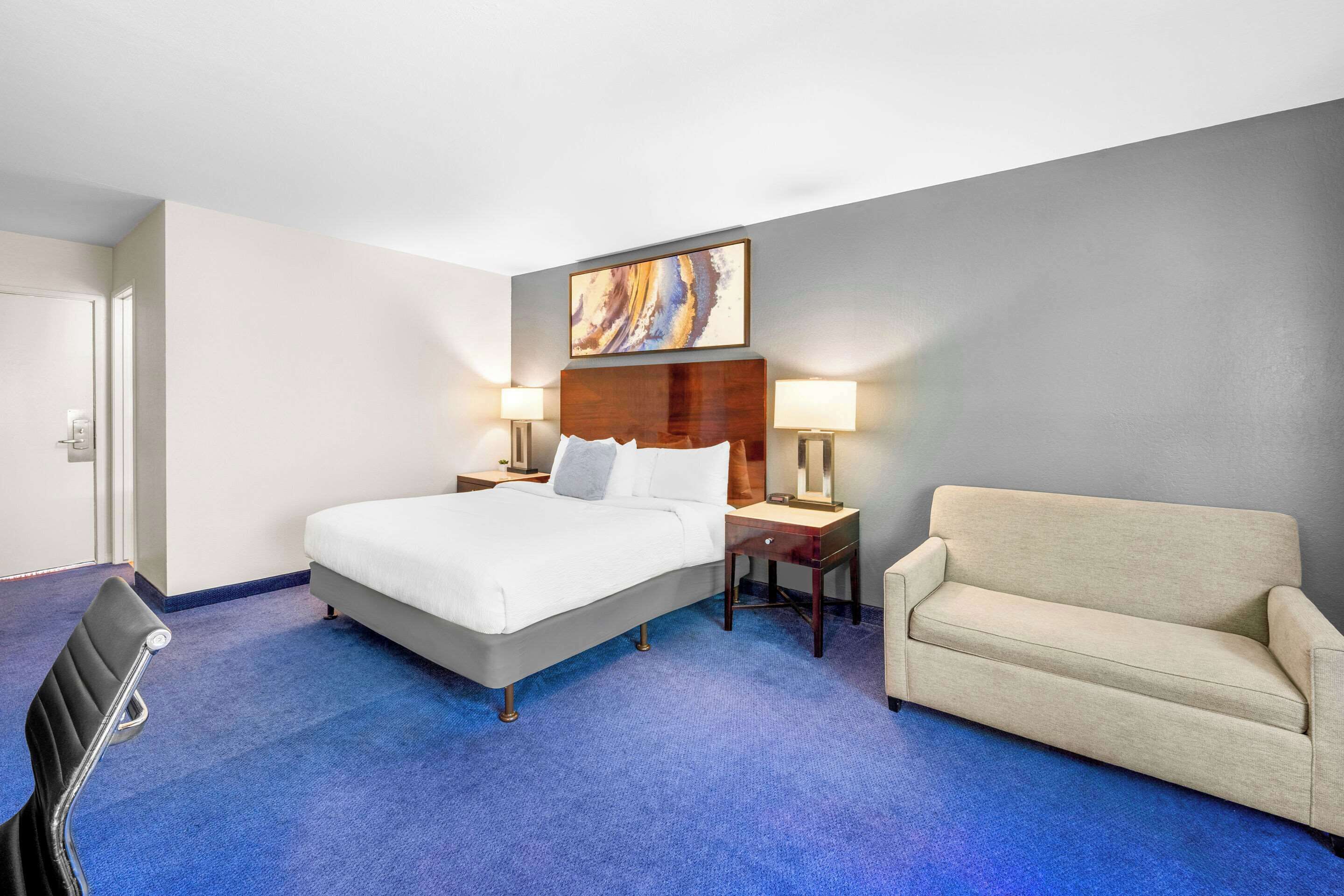 A hotel room with a large bed, a sofa, two bedside tables with lamps, and a painting on the wall.