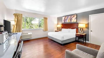 A hotel room with a bed, bedside lamps, a desk with a computer, a chair, and a window with curtains.