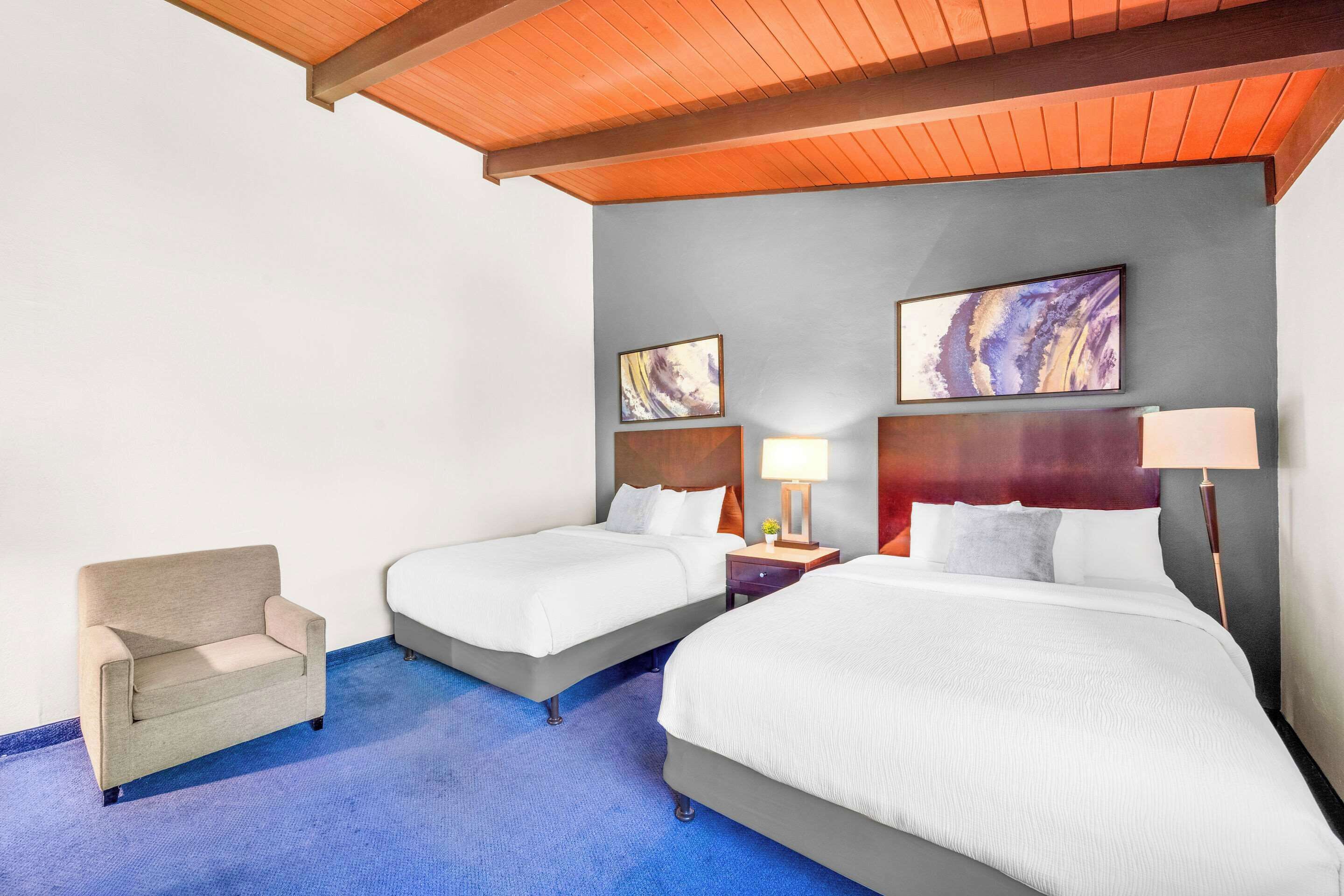 Una habitación de hotel con dos camas, un sofá y obras de arte en las paredes.