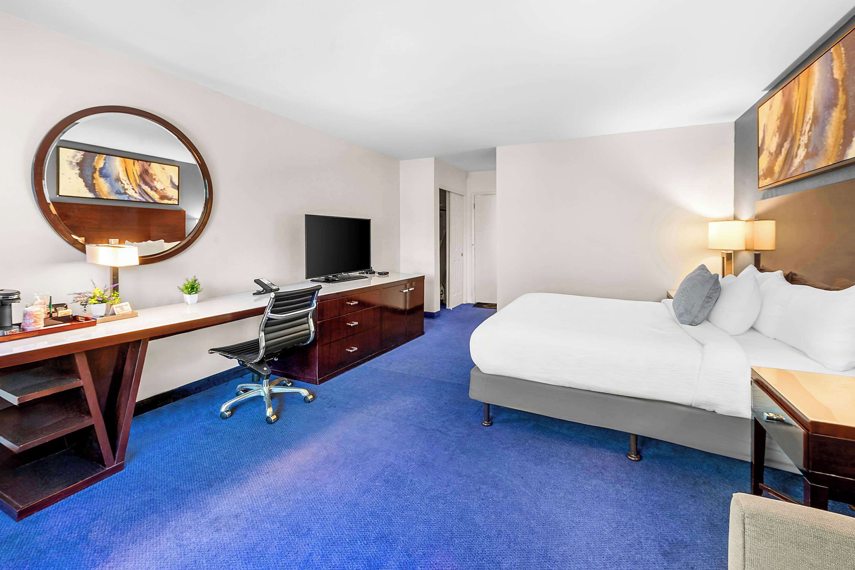 Quarto de hotel com cama, escrivaninha, cadeira, televisão e obras de arte nas paredes.
