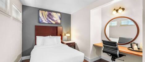 Ein Hotelzimmer mit Bett, Schreibtisch mit Stuhl, rundem Spiegel und einem Bild an der Wand.