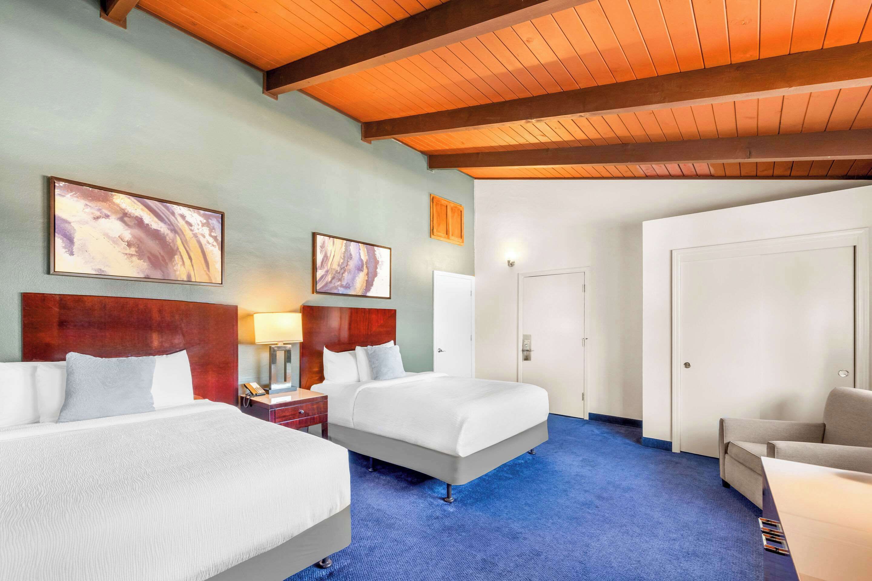 A hotel room with two beds, a wooden ceiling, and a blue carpet.