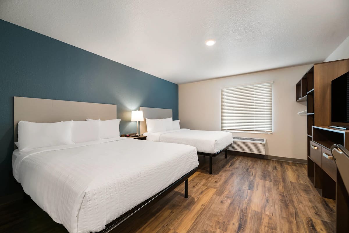A hotel room with two beds, a desk, a chair, a lamp, and a window with blinds.