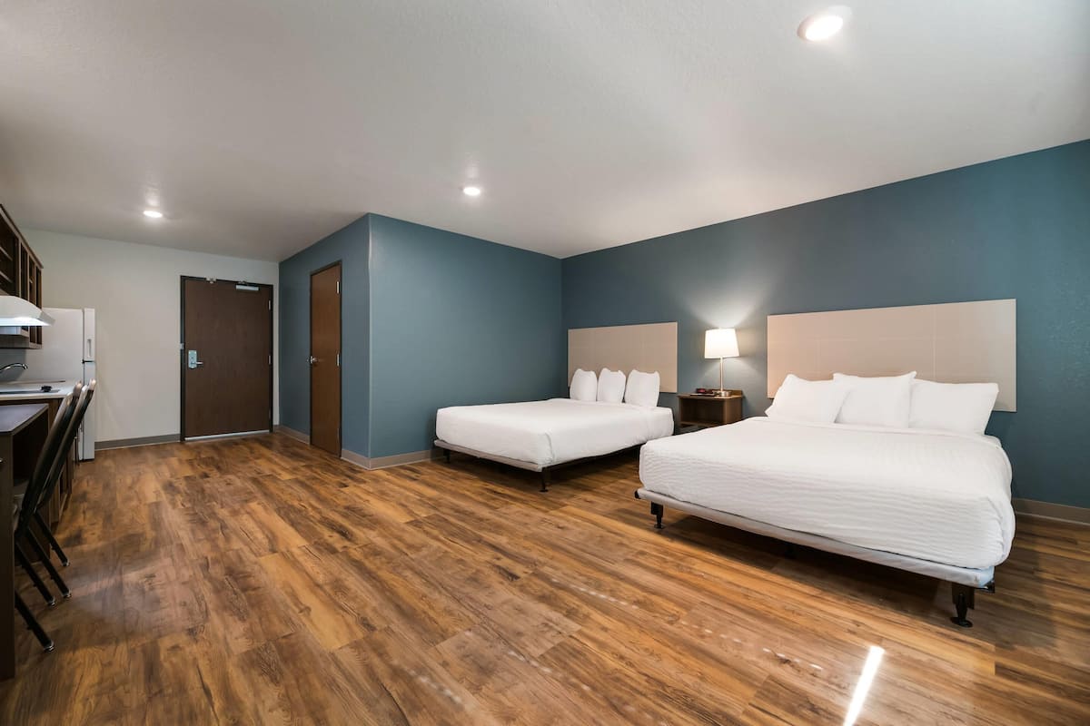 A hotel room with two beds, a desk, and a door.