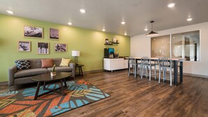 A living room with a sofa, coffee table, and rug, a dining area with a table and chairs, and a kitchen with cabinets and a countertop. - WoodSpring Suites Cocoa Beach - Rockledge (Rockledge)