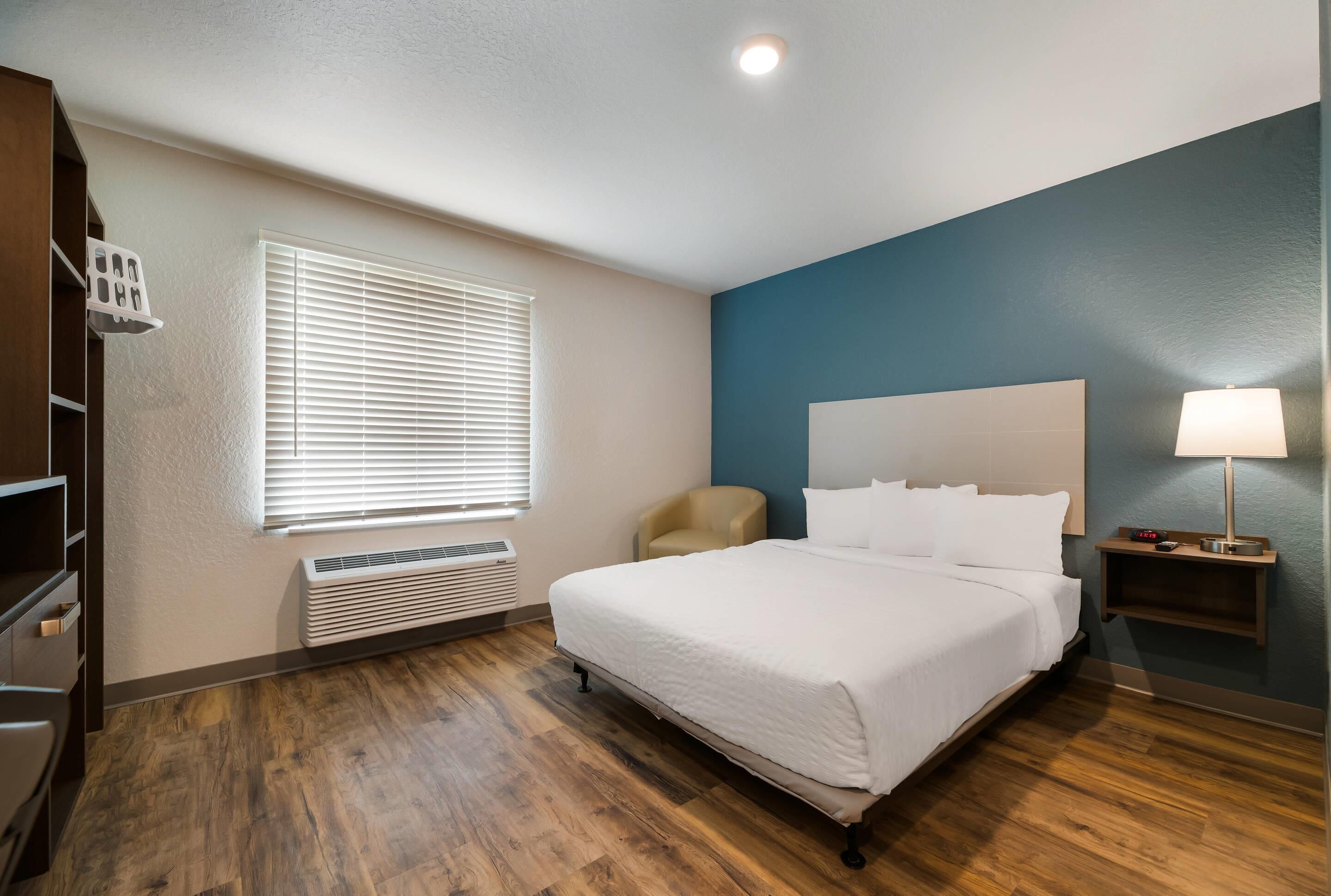 A hotel room with a large bed, a chair, a nightstand, a lamp, and a window with blinds.