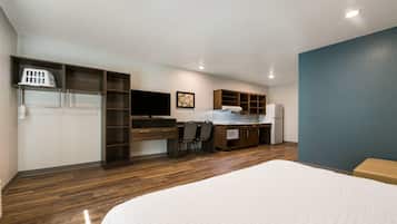 Un dormitorio con una cama grande, un escritorio con silla, un televisor y una kitchenette con refrigerador y microondas.