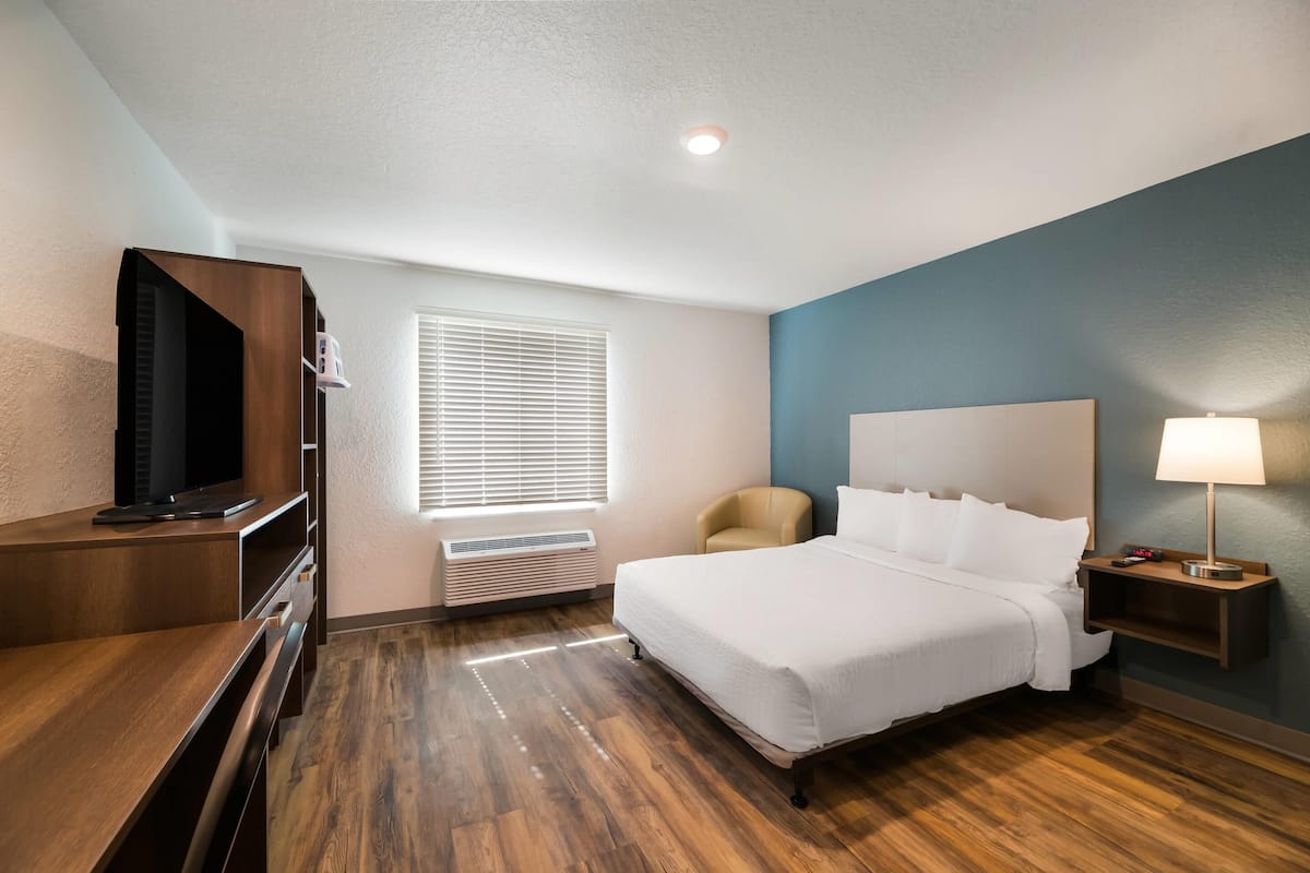 A hotel room with a bed, a TV, a desk, a chair, a lamp, and a window with blinds.